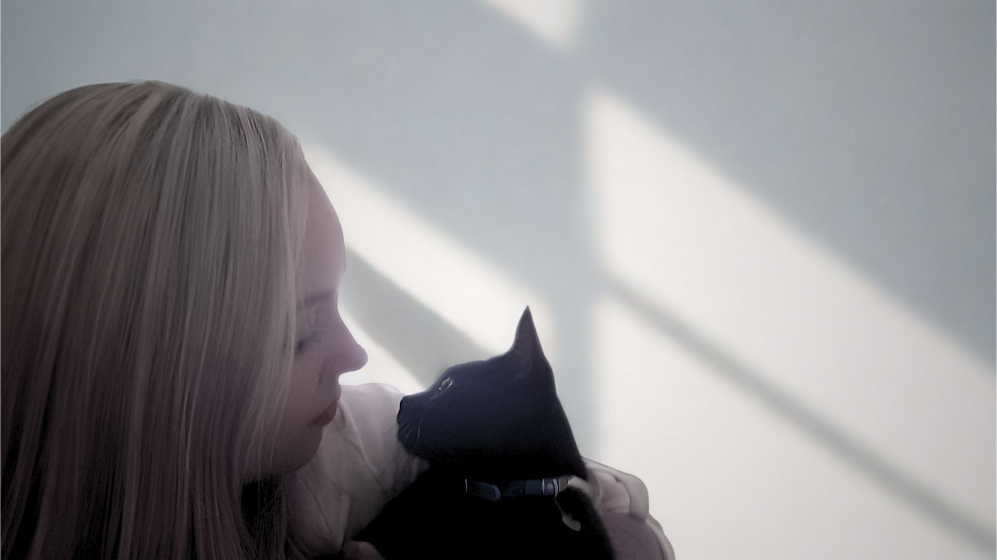 Woman holding a black cat with sunlight casting shadows on a white wall