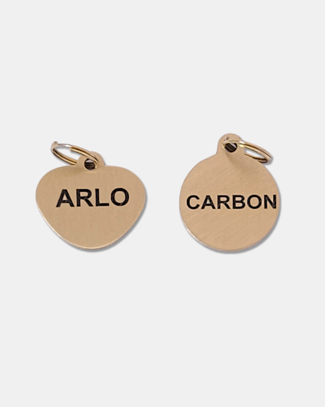 Two brass cat tags with 'ARLO' and 'CARBON' engraved on a white background